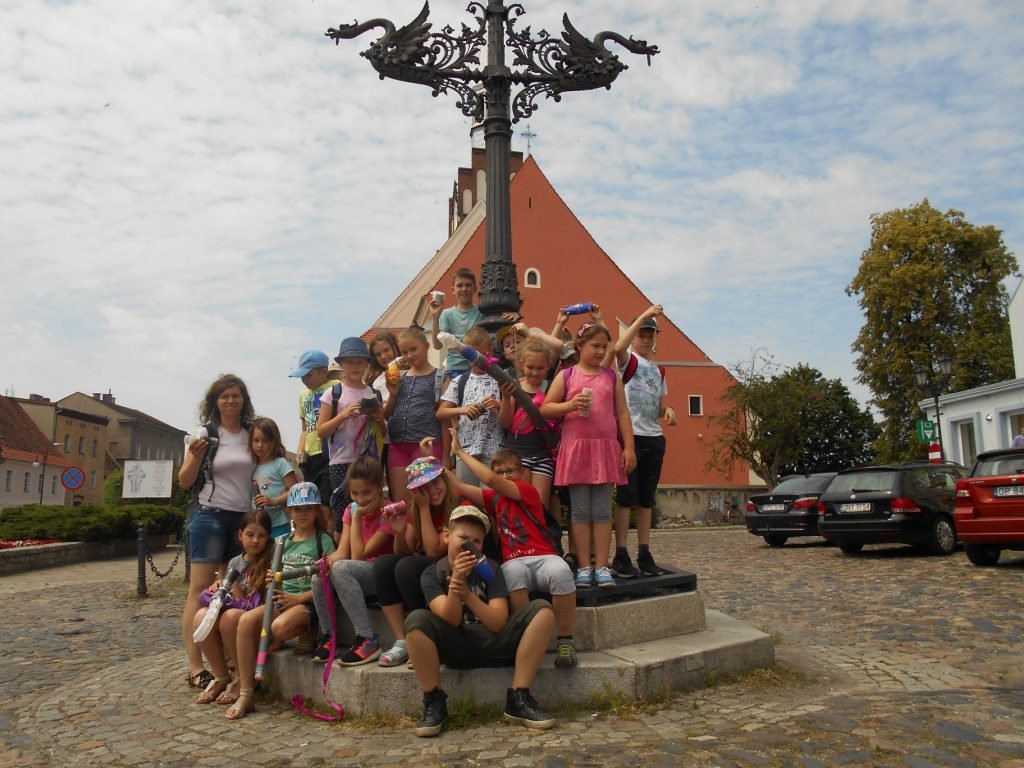 Duża grupa dzieci na cokole wokół kolumny.