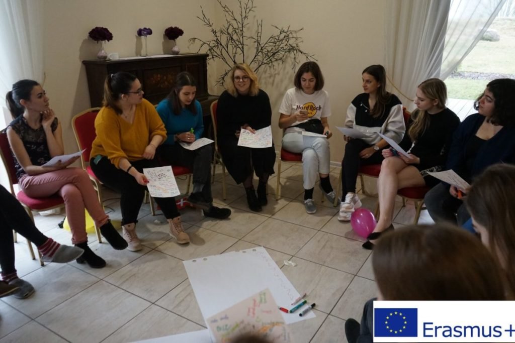 grupa kobiet siedząca w kręgu z kartkami w ręku