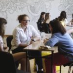 Dwie grupy osób siedzących przy stołach prowadzą rozmowę.