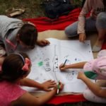 Trójka dzieci siedząca na kocu rysuje na dużym arkuszu papieru.