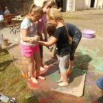 Cztery dziewczynki stoją w kałuży farby boso, trzymając się za ręce.