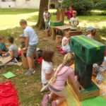 Duża grupa dzieci na trawie i kolorowych kocach buduje zamek z kartonów.