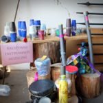 Na szafce stojące kolorowe kubki i butelki z dużą kartką podpisana „Kreatywne instrumenty muzyczne".