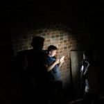 Na zdjęciu chłopak i dziewczyna stoją w ciemności, podświetleni tylko światłem latarki z telefonu.