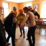 Grupa dorosłych w koronach na głowach z papieru kolorowego stoi w kręgu.