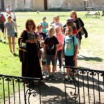 Grupa dzieci z dwoma opiekunkami stoi na placu przy zamku.