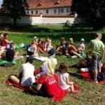 Bardzo duża grupa dzieci siedząca na kocach na trawie podczas słonecznej pogody.