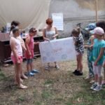 Grupa kilku dzieci wraz z kobietą trzyma duży plakat z różnymi napisami, który same zrobiły.