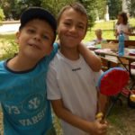 Na pierwszym planie dwóch uśmiechających się chłopców trzymających zabawkę. W tle dwie dziewczynki.