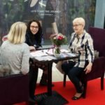 rozmowa trzech kobiet przy stoliku z kwiatami