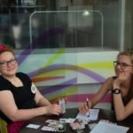 Dwie młode dziewczyny siedzą uśmiechnięte przy stoliku i grają w karty.