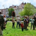 Grupa dzieci, młodzieży i dorosłych przygląda się, jak mała dziewczynka strzela z luku.