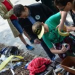 Chłopczyk w czapce ze znakiem batmana z pomocą dwójki dorosłych okleja taśma kawałek plastiku.