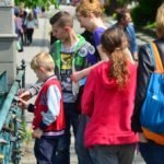 Dwójka chłopców trzyma w rękach kłódkę przypięta do mostu, asystuje im młoda kobieta.