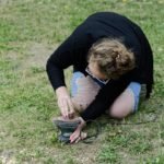 Kobieta klęcząca na trawie wygładza element na szlifierce oscylacyjnej.