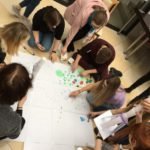 grupa osób tworzy na ziemi duży plakat